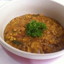 A close up picture of Oats Upma garnished with parsley and served in a white and red bowl.