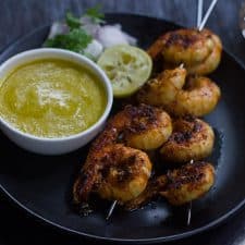 Tandoori Prawns served with mango chutney, onions and lemon in a black plate.