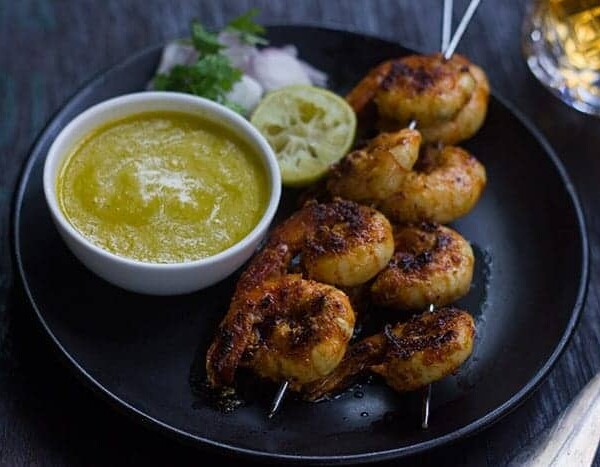 Tandoori Prawns served with mango chutney, onions and lemon in a black plate.