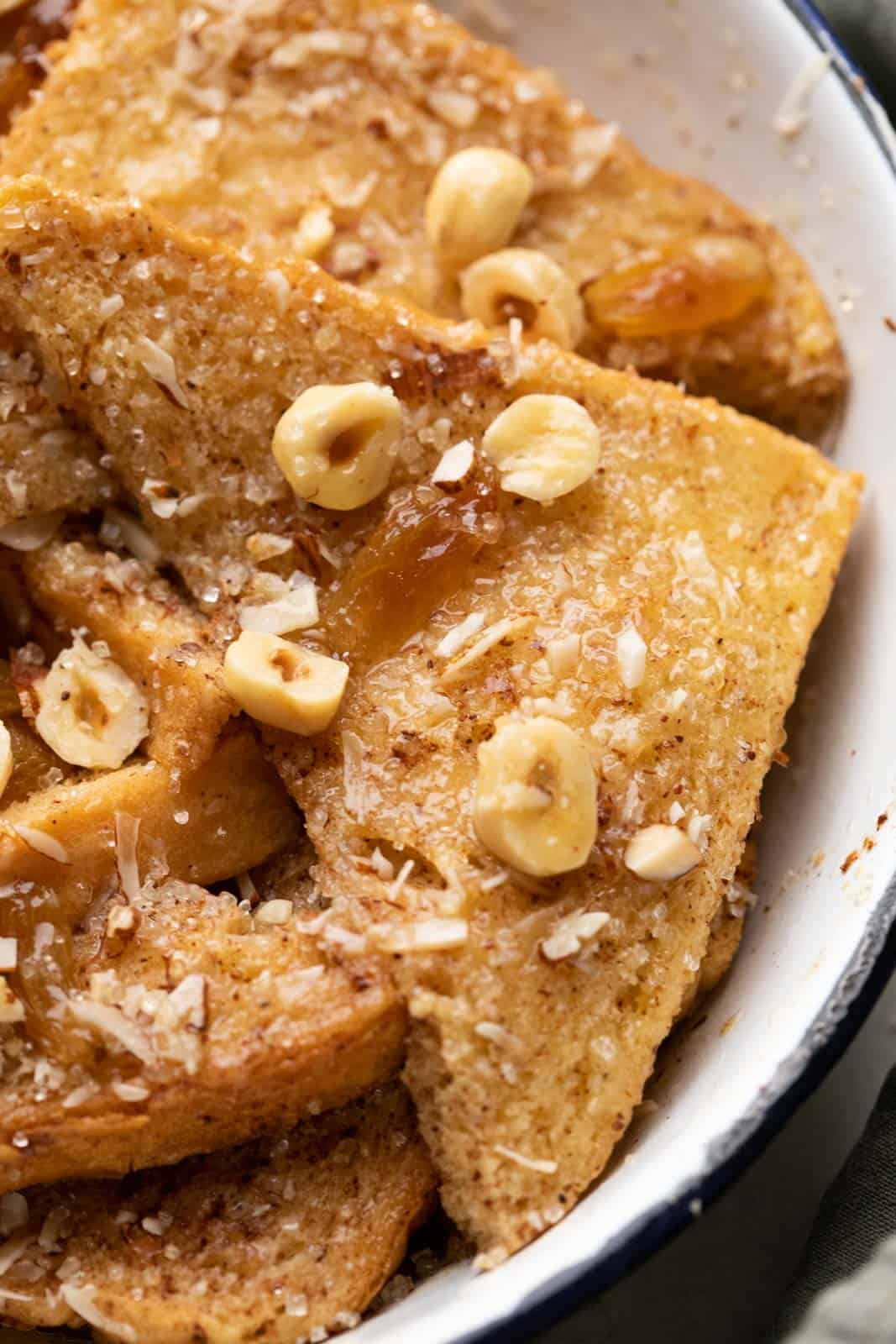 Closeup of a slice of bread from the bread pudding to show the beautiful texture thats glistening with melted butter and is topped with nuts and raisins