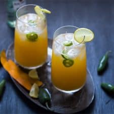 Tall Mango Jalapeno Fizzy Cocktail served with ice and a slice of lime in glasses resting on a brown tray.