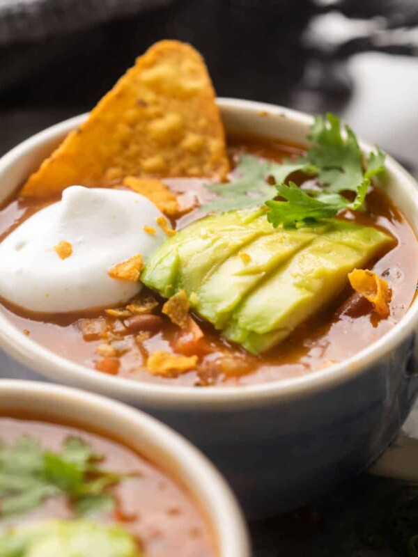 Picture of mexican soup served in a bowl topped with avocado, cilantro, sour cream and tortilla chips