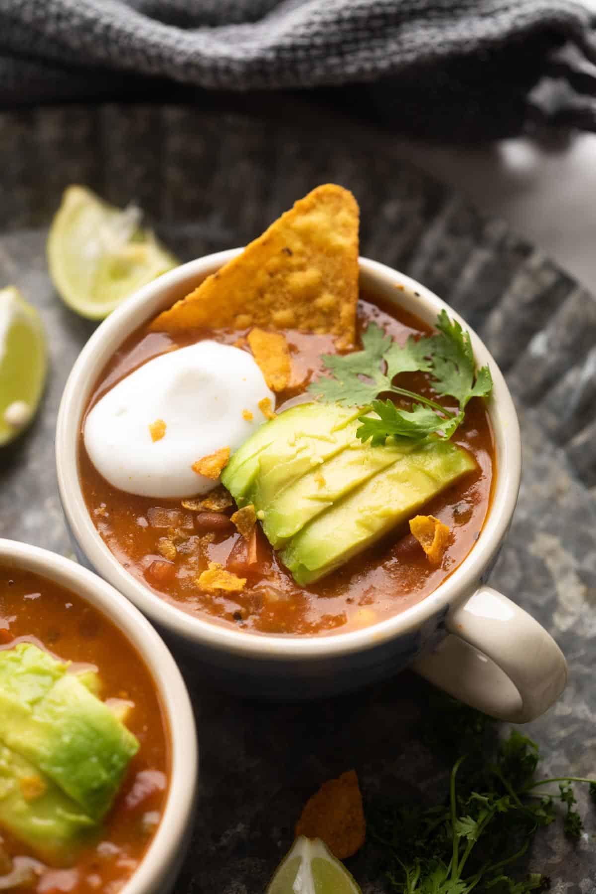 Picture of mexican soup served in a bowl topped with avocado, cilantro, sour cream and tortilla chips