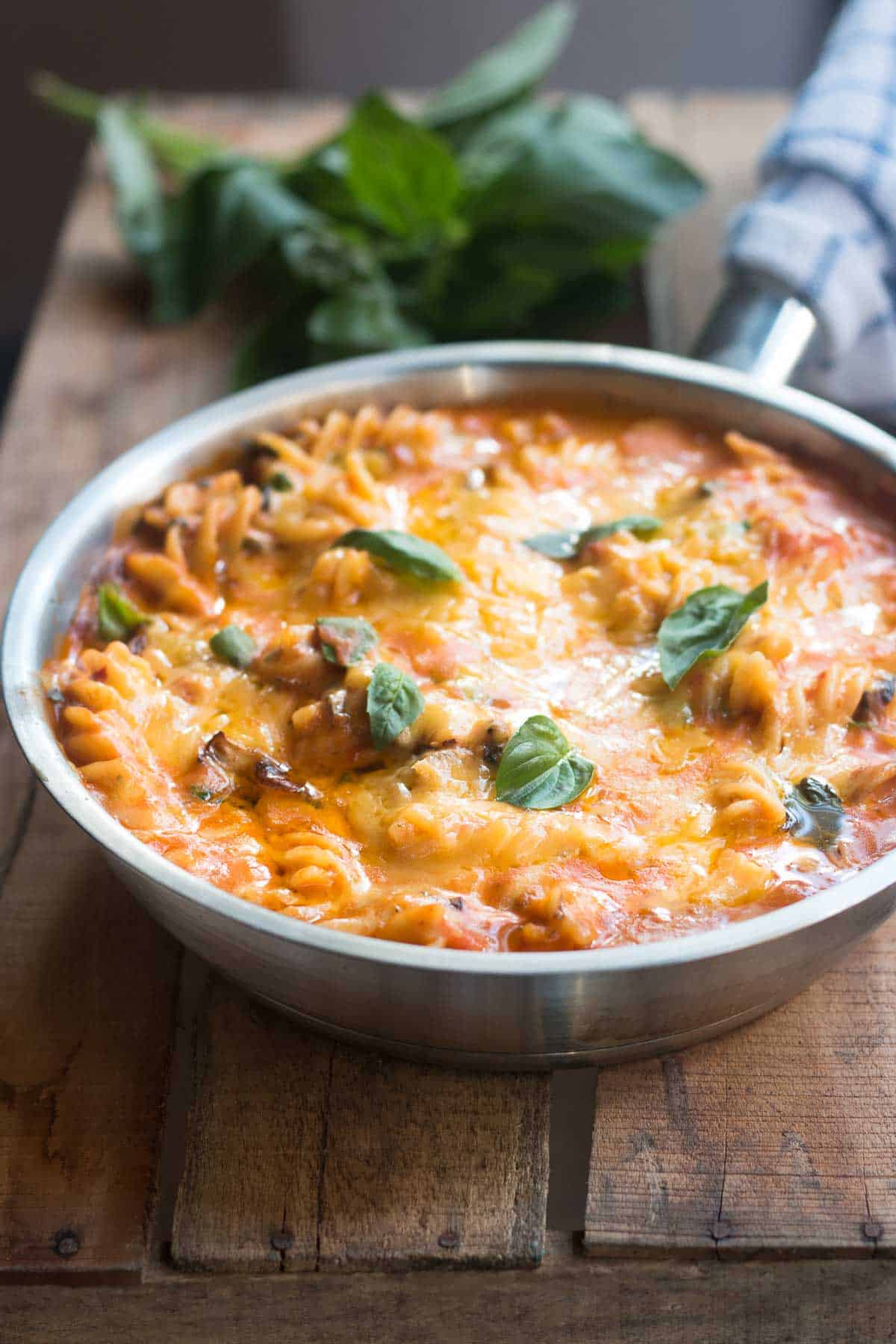 All-In Sunday Veggie Pasta layered with warm, melted cheese and garnished with fresh basil in a skillet.