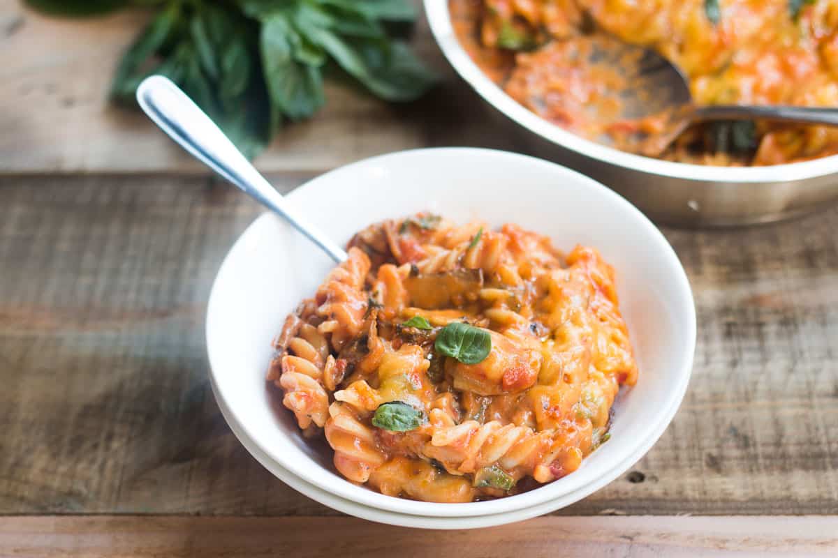 A comforting bowl of cheesy Sunday Veggie Pasta garnished with fresh basil and served in a white bowl.