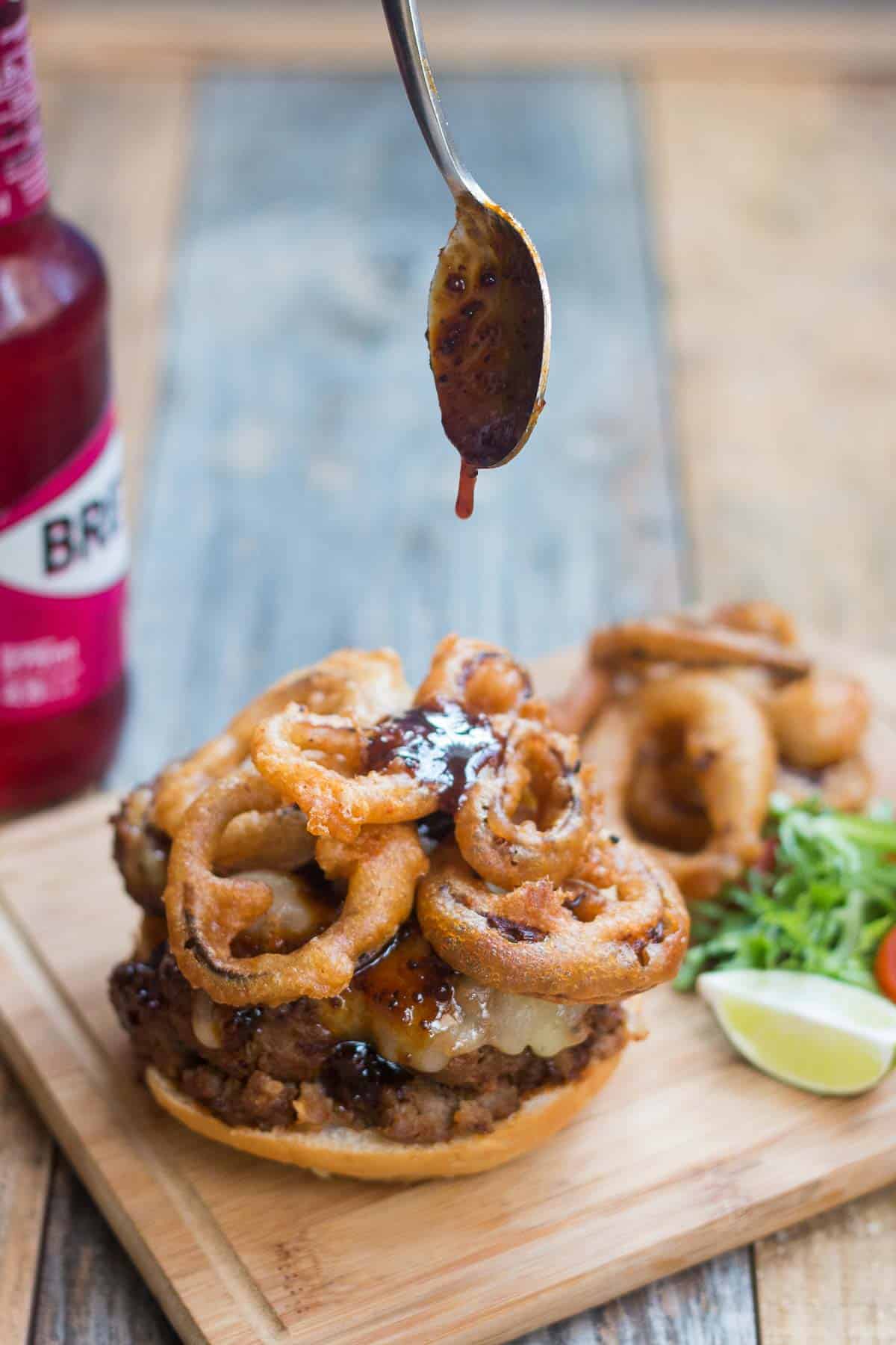 Whiskey sauce being poured over the onion rings in the burger.