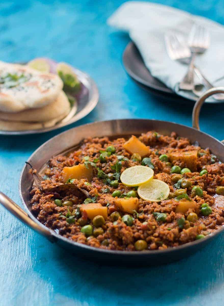 mutton keema in a kadhai with limes, chopped onion and naan on the side