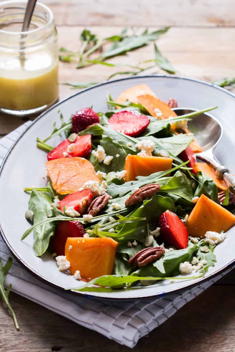 Greens, Persimmon Ricotta Salad with Orange Dressing served in a white plate