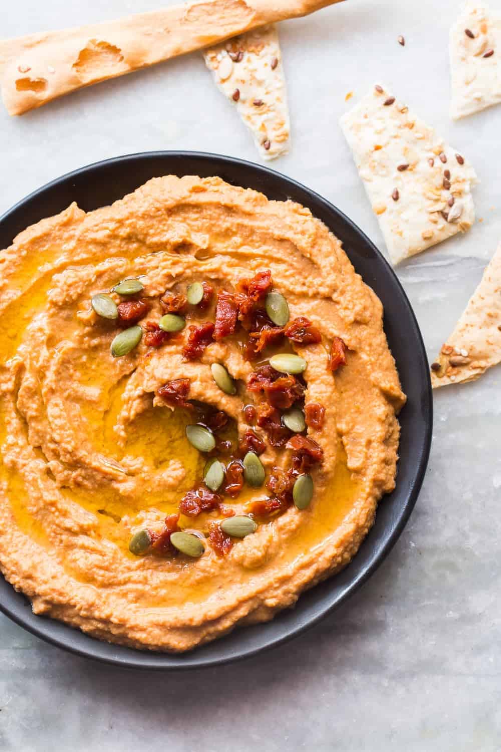 top shot of creamy sundried tomato hummus in a black bowl with lavash on the side