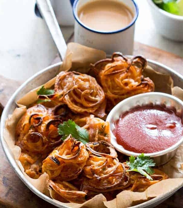 Crispy Baked Onion Pakodas (Fritters) garnished with coriander and served with sauce and chai.