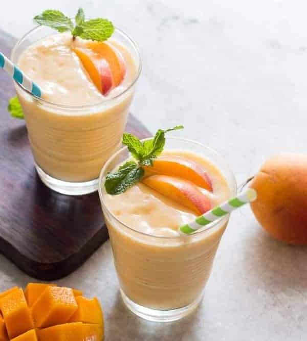 Healthy Vegan Frozen Peach Mango Smoothie garnished with mint leaves and served with straws.
