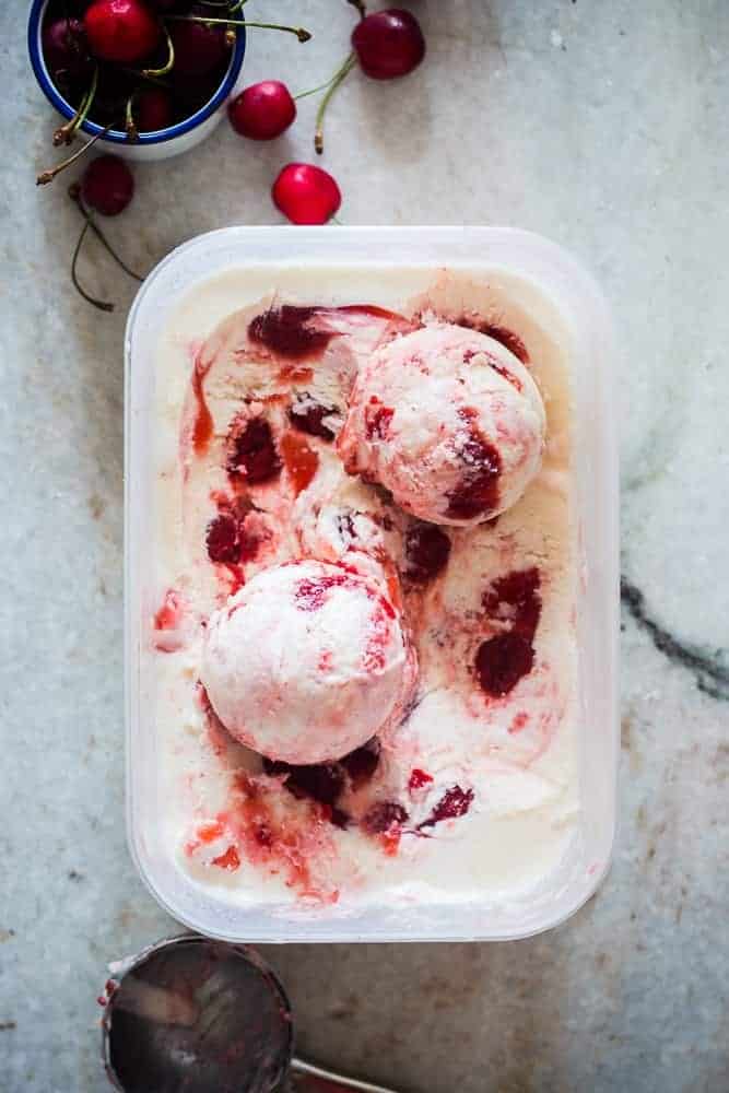 lychee cherry swirl icecream in a white tub with cherries on the side