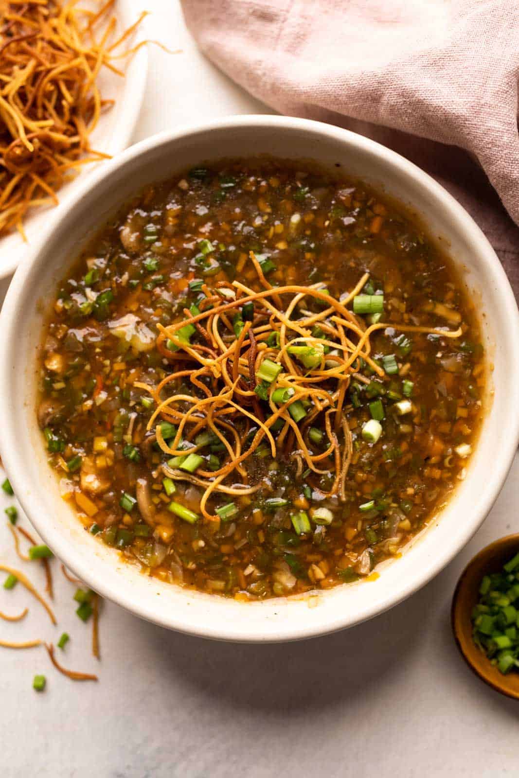 Chicken Manchow soup served in a white bowl topped with fried noodles and spring onions