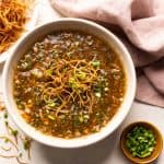 Chicken Manchow soup served in a white bowl topped with fried noodles and spring onions