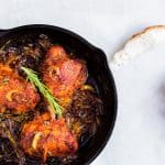 Chicken thighs garnished with rosemary in a black skillet.