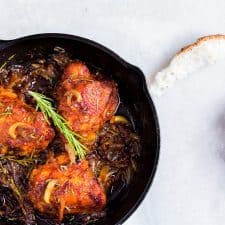 Chicken thighs garnished with rosemary in a black skillet.