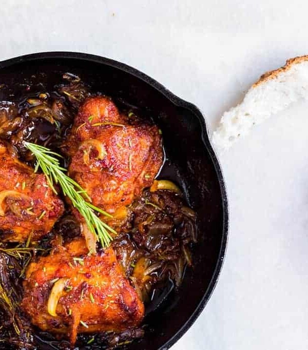 Chicken thighs garnished with rosemary in a black skillet.