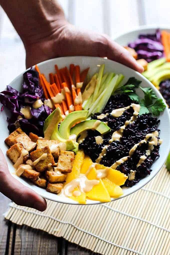 A collection of 13 insanely delicious savoury mango recipes that are sure to blow your mind if you've always had mangoes in sweet dishes. These recipes combine the juicy sweetness of mangoes with savoury ingredients to create a dish that's truly stellar and unforgettable! #spring #mango #recipes #easter #summer #fruit Tofu and forbidden rice bowls being held in a hand
