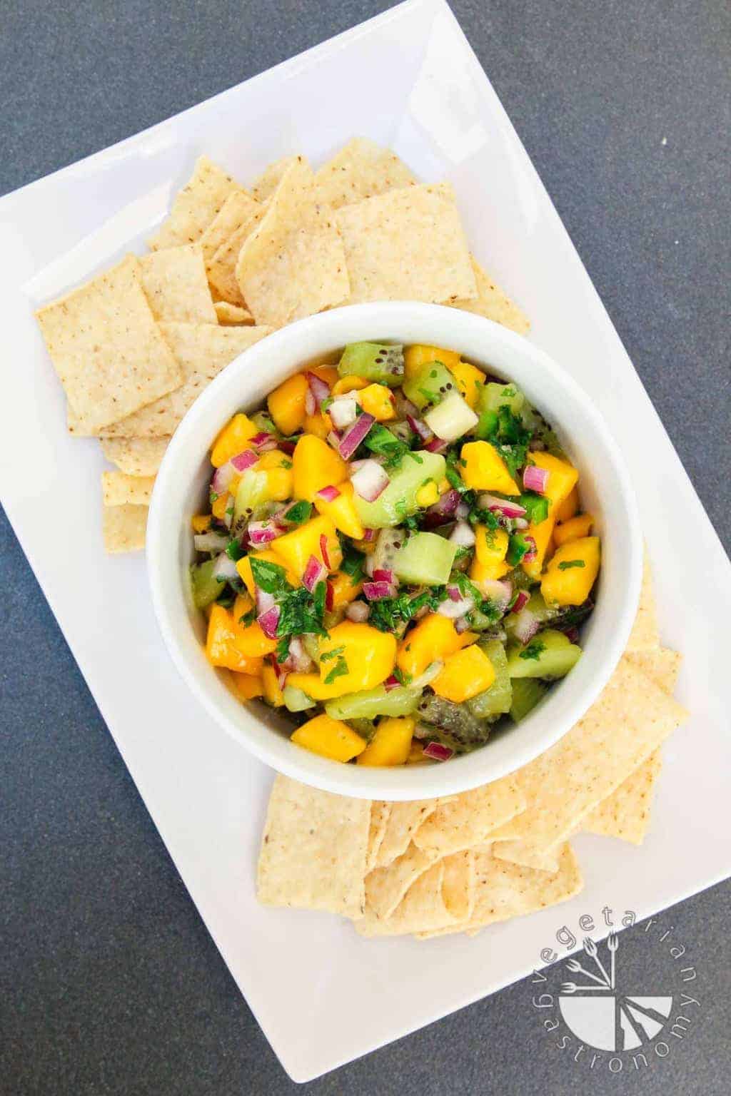 A collection of 13 insanely delicious savoury mango recipes that are sure to blow your mind if you've always had mangoes in sweet dishes. These recipes combine the juicy sweetness of mangoes with savoury ingredients to create a dish that's truly stellar and unforgettable! #spring #mango #recipes #easter #summer #fruit Kiwi Mango Salsa on a white plate with chips