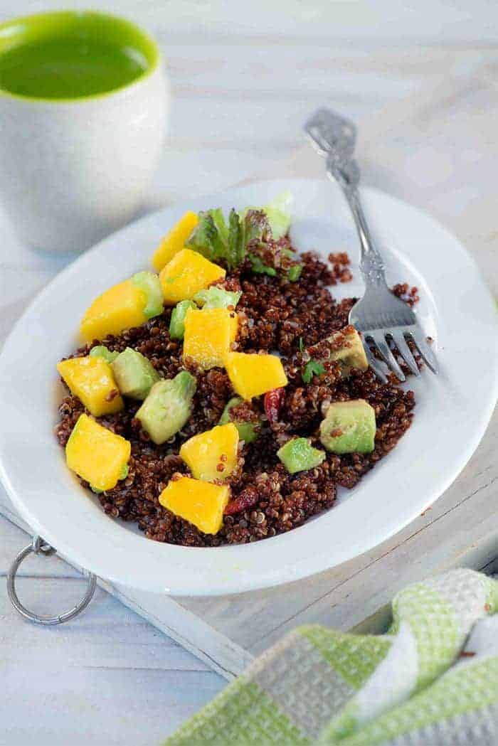 A collection of 13 insanely delicious savoury mango recipes that are sure to blow your mind if you've always had mangoes in sweet dishes. These recipes combine the juicy sweetness of mangoes with savoury ingredients to create a dish that's truly stellar and unforgettable! #spring #mango #recipes #easter #summer #fruit Red quinoa mango salad in a white deep plate with a fork and a glass of water