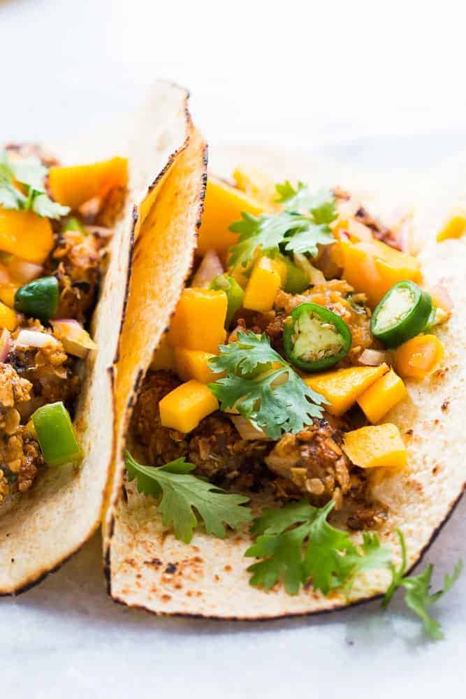 A collection of 13 insanely delicious savoury mango recipes that are sure to blow your mind if you've always had mangoes in sweet dishes. These recipes combine the juicy sweetness of mangoes with savoury ingredients to create a dish that's truly stellar and unforgettable! #spring #mango #recipes #easter #summer #fruit Two fish tacos with mango salsa on a marble countertop