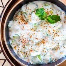 Indian Spiralized Cucumber Mint Raita garnished with some mint, masala and served in a black bowl.