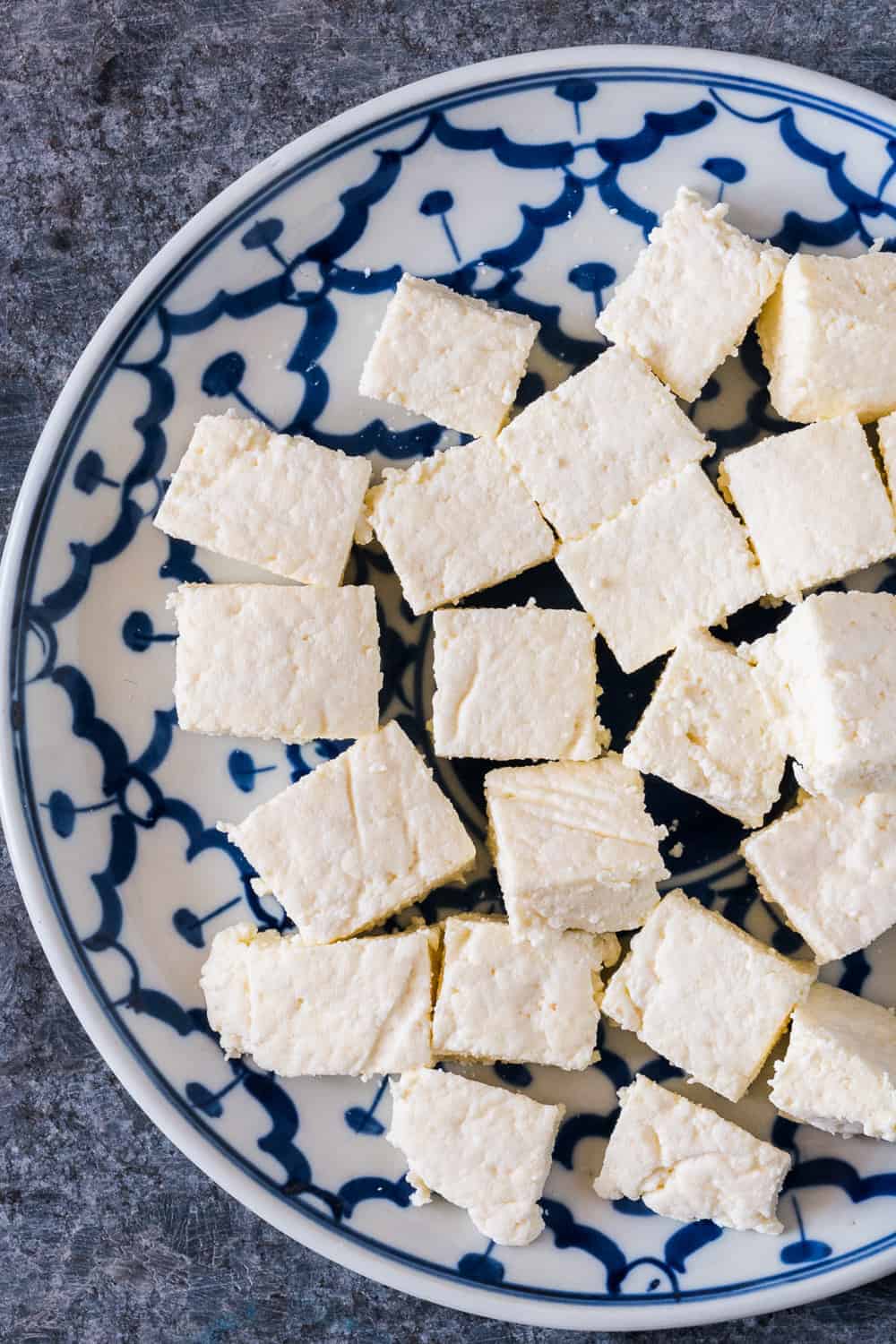 Fresh, homemade paneer cut into cubes on a white and blue plate.