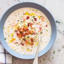 Creamy Cauliflower Chowder topped with bacon, olive oil and served in a bowl.