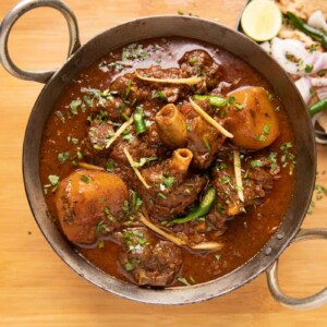 Mutton Curry served in a kadhai with tandoori roti and onions on the side