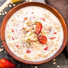 Healthy Strawberries and Cream Breakfast Oatmeal drizzled with honey, chia seeds and served in a wooden bowl.