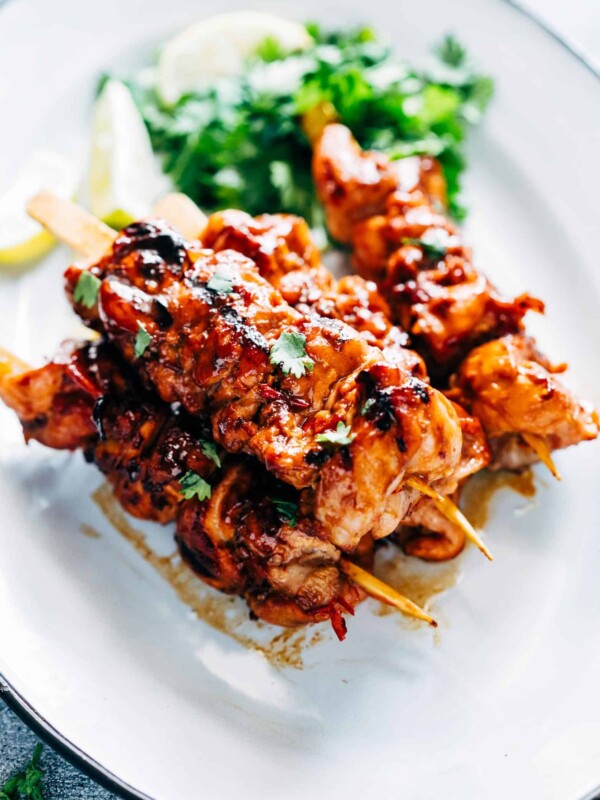 Grilled Sambal Chicken Skewers served with lemon slices and coriander on a white plate.