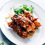 Grilled Sambal Chicken Skewers served with lemon slices and coriander on a white plate.
