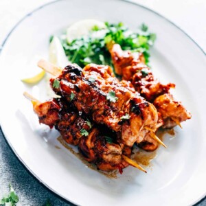 Grilled Sambal Chicken Skewers served with lemon slices and coriander on a white plate.
