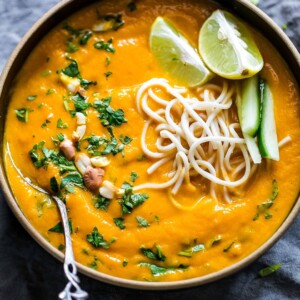 Thai Ginger Carrot Soup garnished with lemon, crushed peanuts, noodles and cilantro and served in a black bowl.