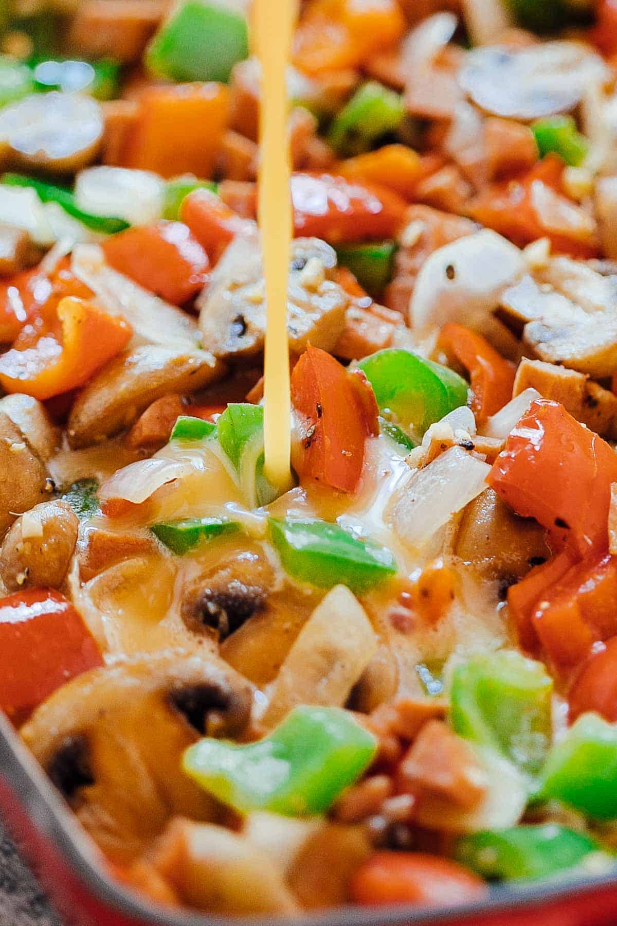 Pouring whisked egg over onions, peppers, mushrooms and ham for the baked denver omelet breakfast casserole