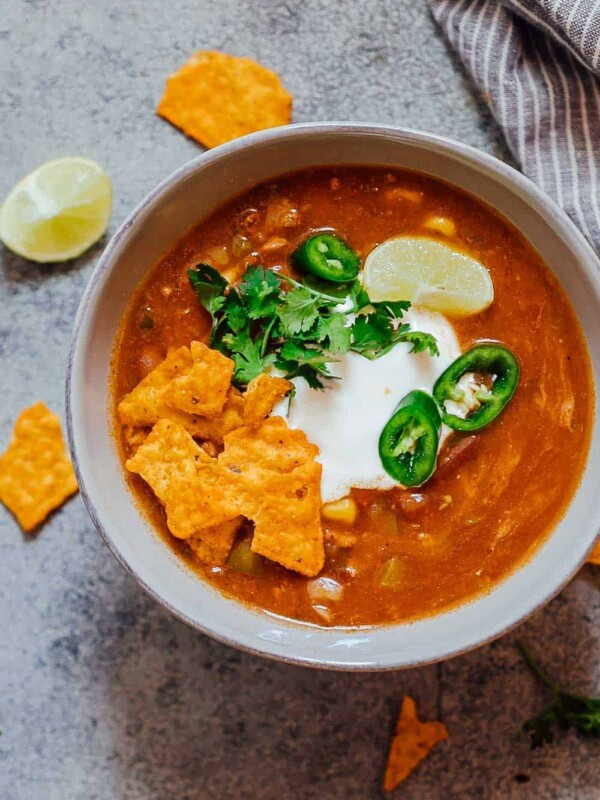 Bowl of chicken enchilada soup made in the Instant Pot topped with sour cream, cilantro, sliced jalapenos, tortilla chips and a lime wedge