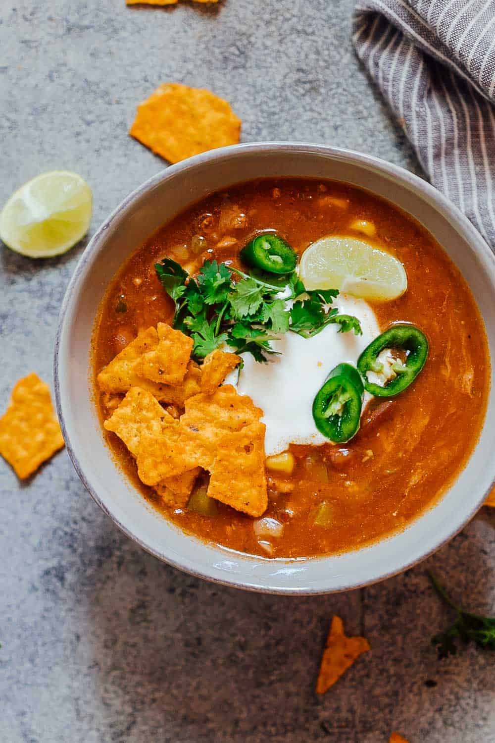 Bowl of chicken enchilada soup made in the Instant Pot topped with sour cream, cilantro, sliced jalapenos, tortilla chips and a lime wedge