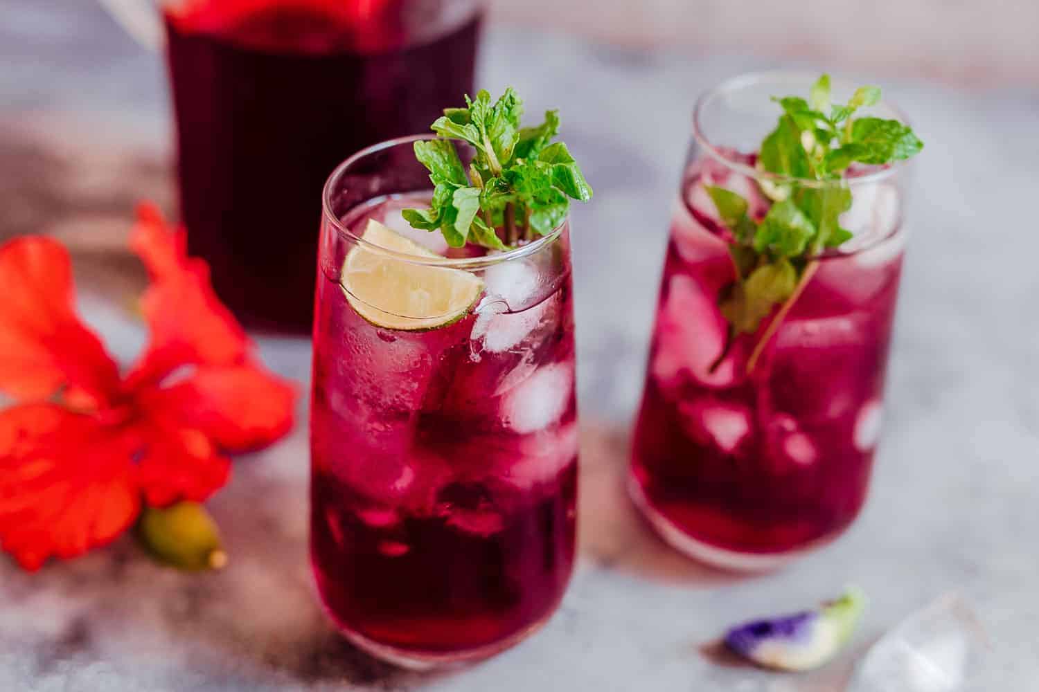 Learn how to make hibiscus tea which has some amazing benefits. Make this with either fresh or dried flowers and choose to have it as a hot cup of tea or as hibiscus iced tea because either way it's delicious and really good for you! #hibiscus #healthfood #drink #icedtea #summer #recipe Glasses of iced hibiscus tea