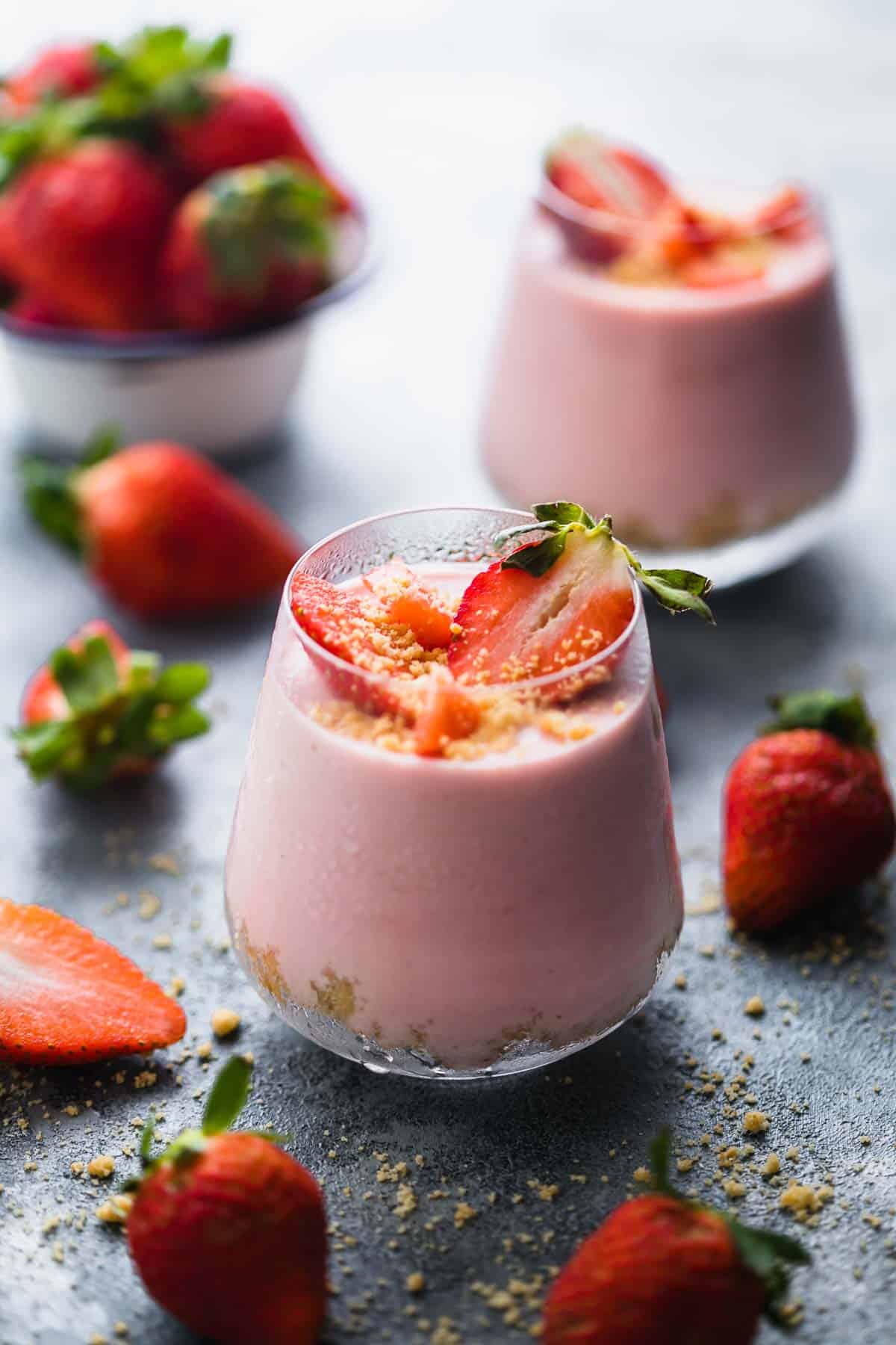 Two No Bake Strawberry Cheesecake Jars with fresh strawberries scattered around