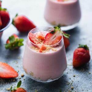 Two No Bake Strawberry Cheesecake Jars with fresh strawberries scattered around