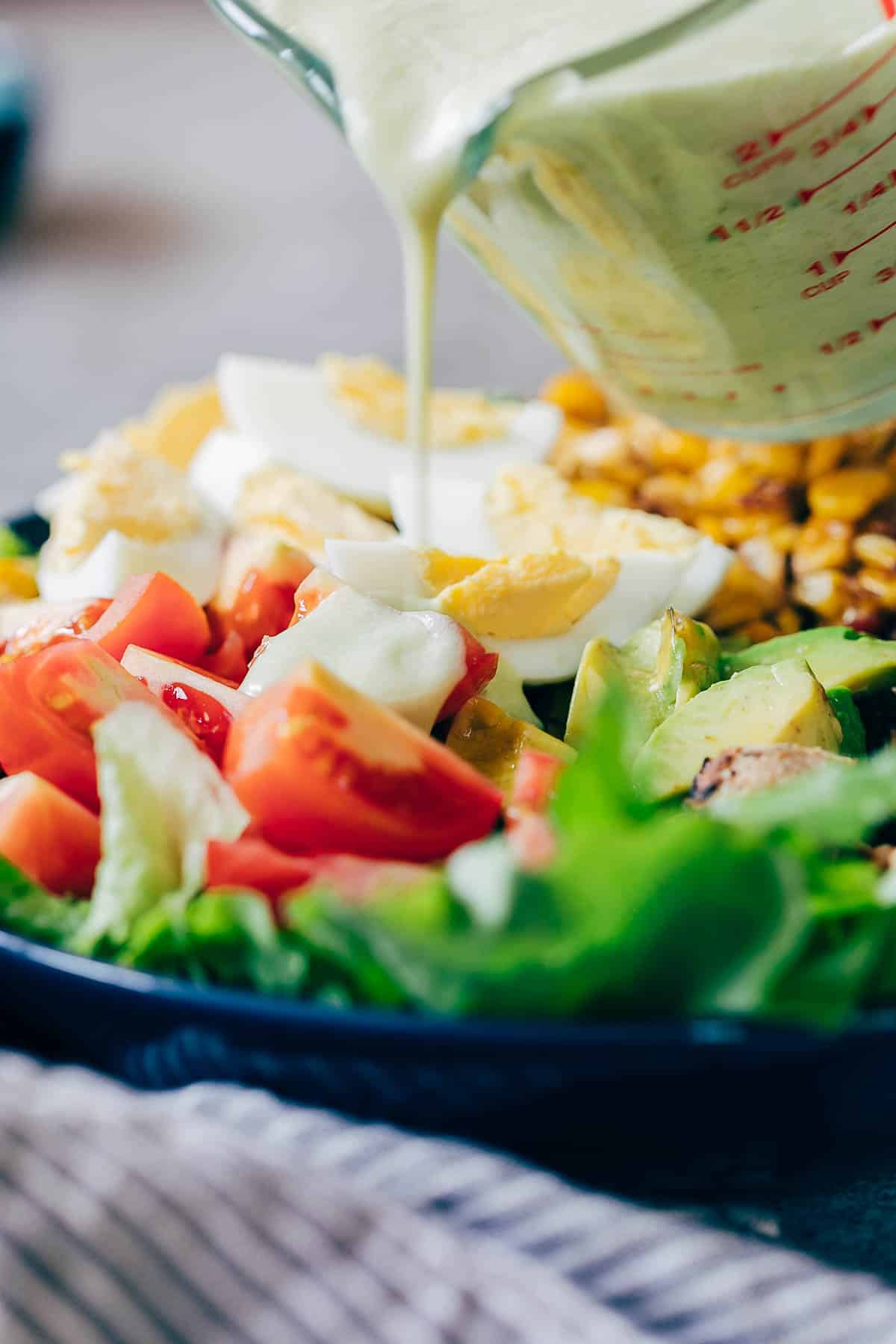 Creamy avocado blue cheese salad dressing is the best homemade blue cheese dressing you'll try - its lighter because it's yogurt based and has a sharp taste that's perfect when drizzled on your favourite cobb salad. You can use this dressing to a pasta salad or even use it as a dip! creamy avocado blue cheese dressing being poured on cobb salad