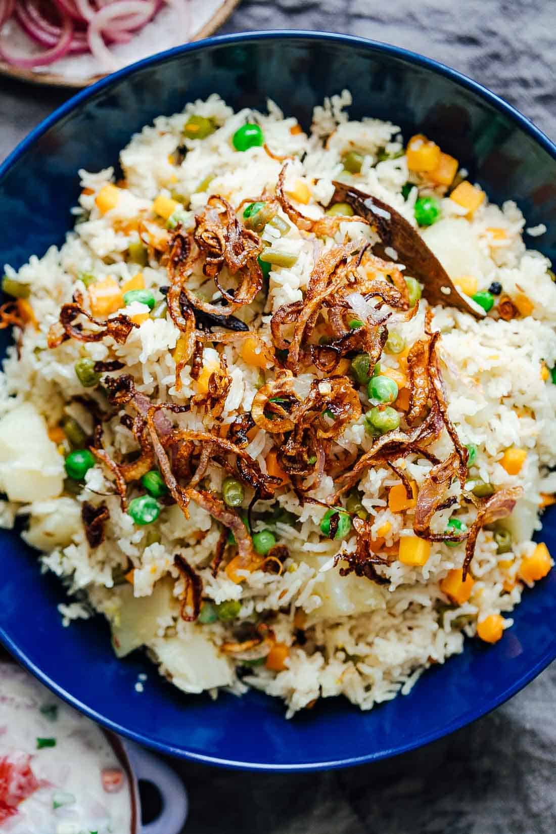 Pressure cooker veg pulao served in a bowl with crispy onions on top