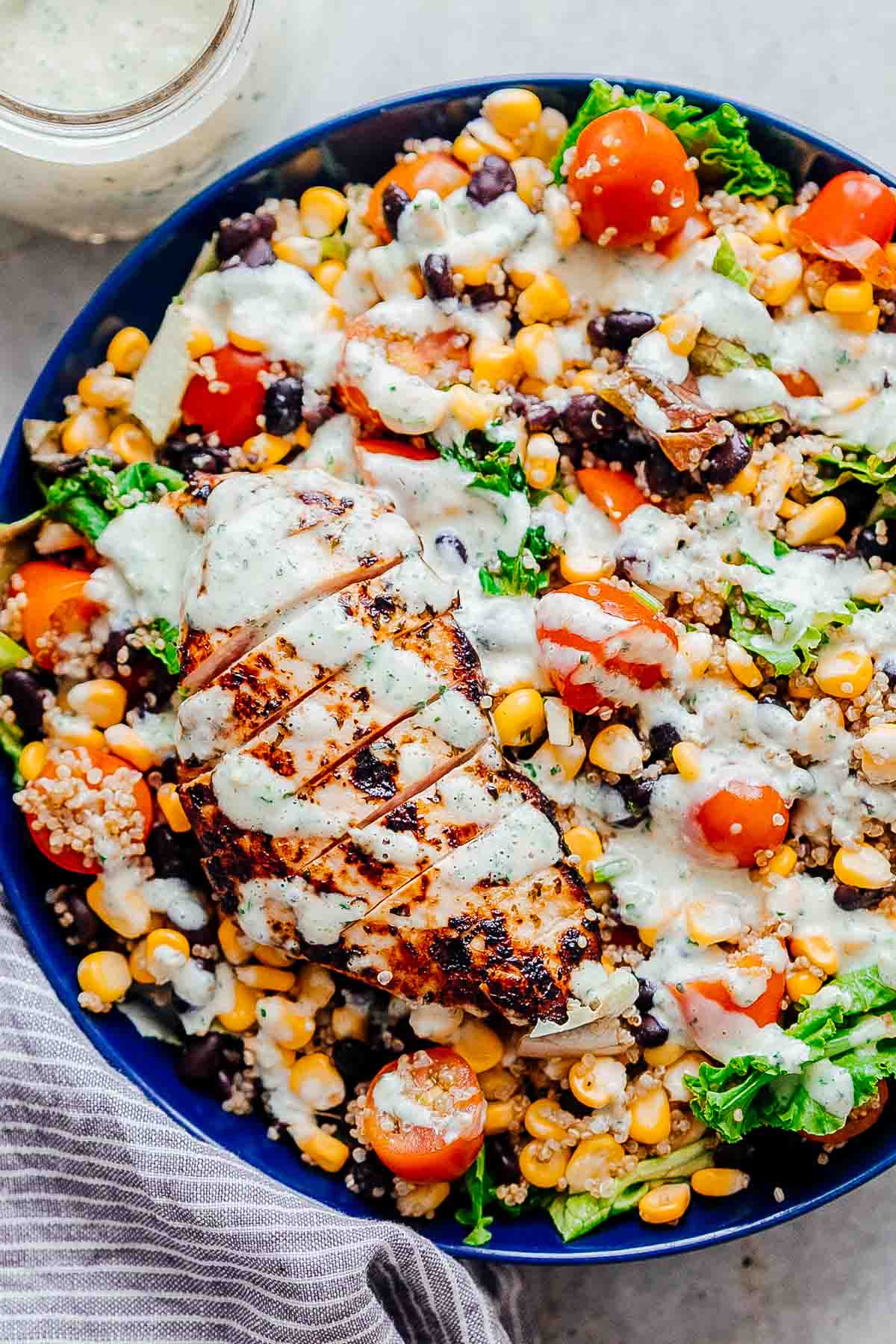Southwest chicken quinoa bean salad in a blue bowl drizzled with a creamy cilantro greek yogurt and sour cream dressing