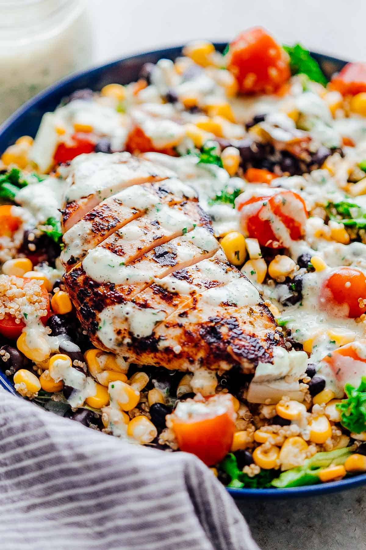 Southwest Chicken Quinoa Bean Salad is a hearty, delicious salad that's more like a meal. I have two dressing recipes for you to choose from - cilantro lime and a creamy southwest dressing with yogurt and sour cream. This salad recipe is a keeper for warm summer months! #salad #healthy #southwest #dinner Closeup of dressing drizzled on southwest chicken quinoa bean salad