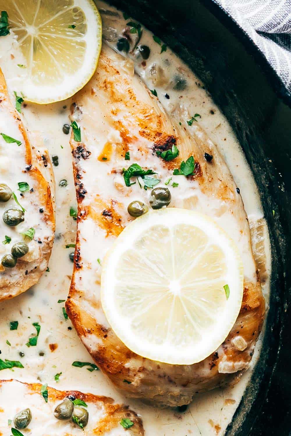 LEMON CHICKEN SCALLOPINI is a super quick, healthy and fast dinner recipe that takes less than 30 minutes to put on the table and has a delicious lemon sauce that you'll want to drink straight from the pan! Studded with capers, this dish looks fantastic. Its gluten free and keto friendly. #fastdinner #chicken #lunch #lemon #summer Closeup of creamy lemon chicken scallopini with lemon slices and capers on top