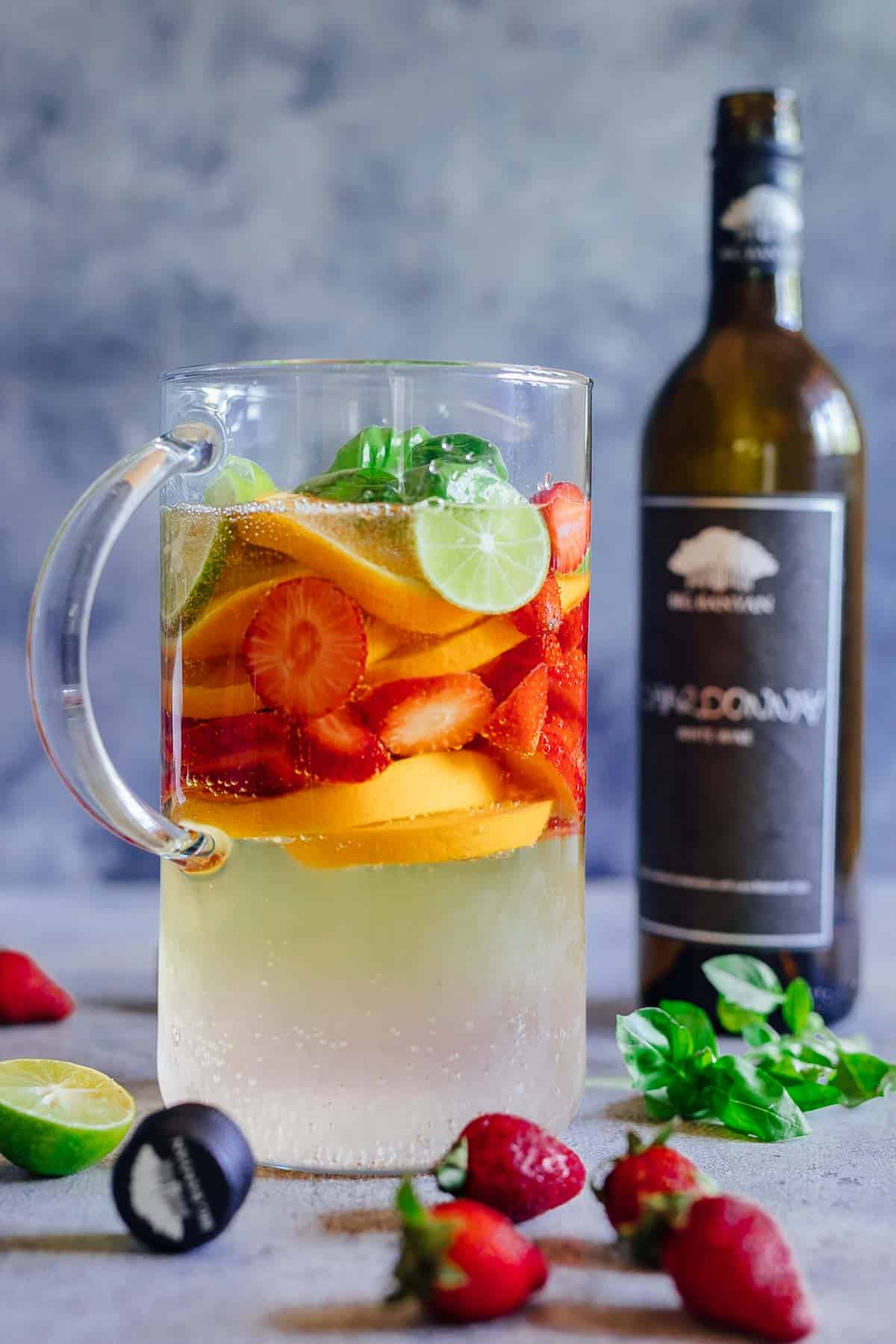 Strawberry Orange White Wine Sangria is a refreshing cocktail that combines the sweetness and flavours of strawberries, oranges, limes and basil with white wine for a fresh take on a traditional sangria. It's the perfect brunch drink that can be made ahead for a crowd. #whitesangria #redwine #cocktails #recipe #drink #summer A pitcher of strawberry orange white wine sangria with a bottle of chardonnay in the background