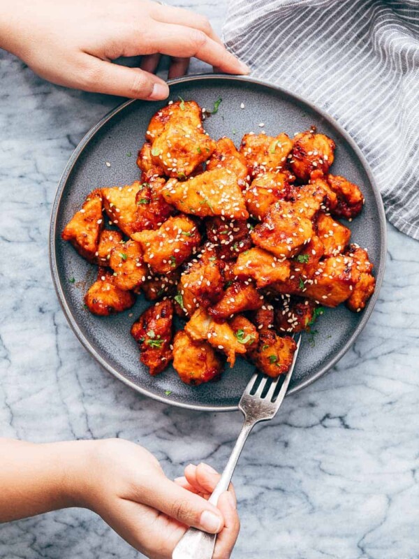 Korean Popcorn Chicken on a plate with a hand coming up to take a bite with a fork