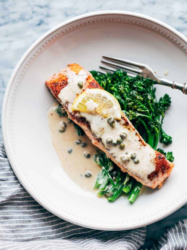 Creamy Salmon Piccata with creamy Lemon Sauce served with greens on a white plate.