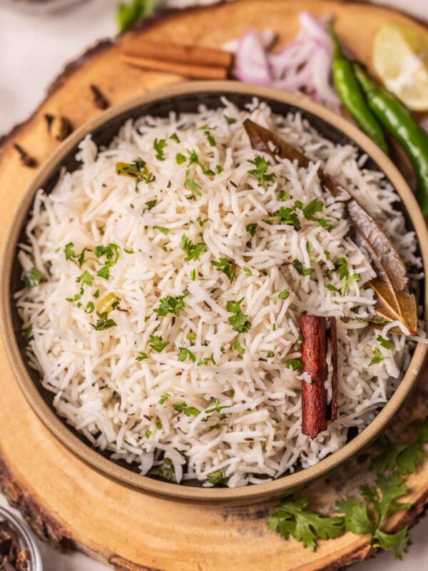 jeera rice served in a bowl, which is placed on a wooden platter with lemon wedges, onions, and green chillies