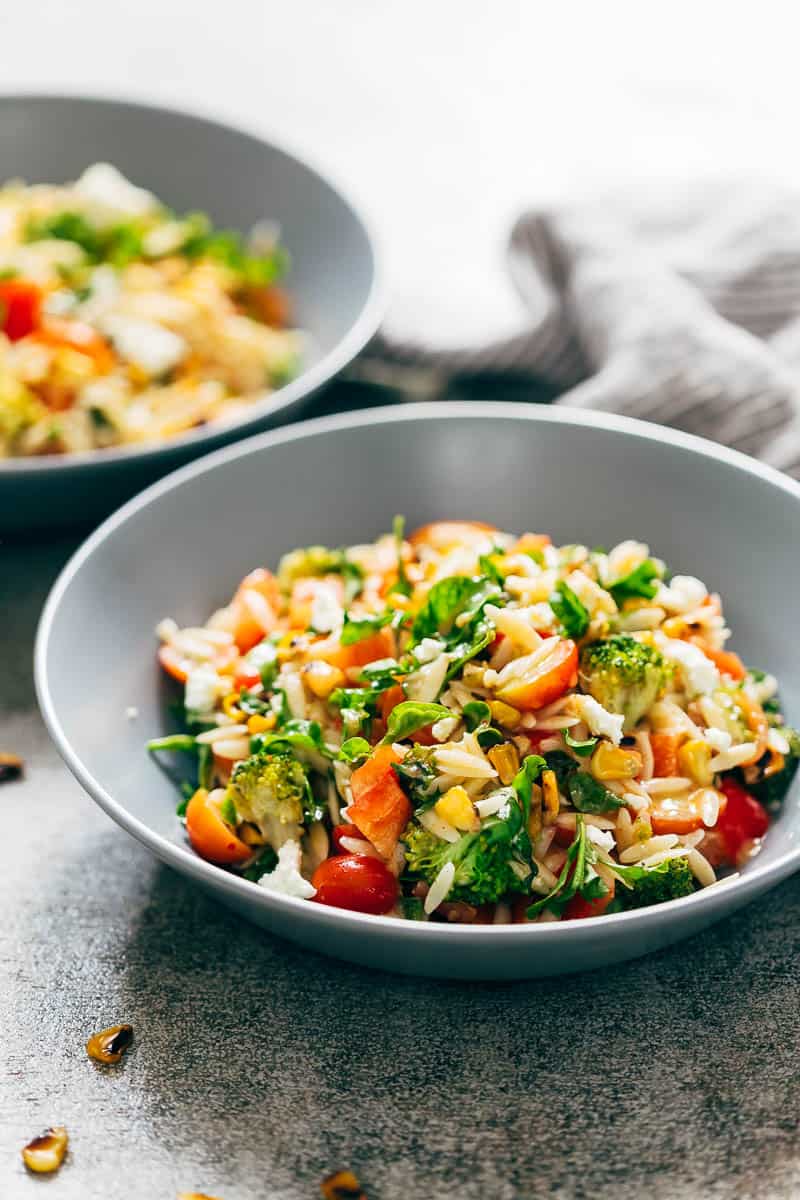 Lemon orzo pasta salad is loaded with veggies, and tossed in a zippy lemon dressing. This vegetarian salad should be made ahead to let the flavours combine. Easily made vegan and perfect for a crowd. #salad #pasta #picnicrecipes #potluck #barbecue #cleaneating #lunch Closeup of lemon orzo pasta salad served in grey bowls